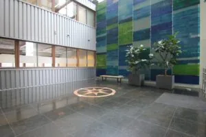 Moderne entreehal aan de De Ruijterkade met een grote wanddecoratie, twee plantenbakken, een bankje en een kompasroos op de vloer.